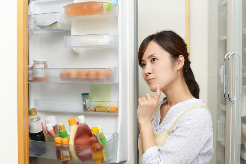 冷蔵庫の中を見ながら、ごはんの献立を考える女性