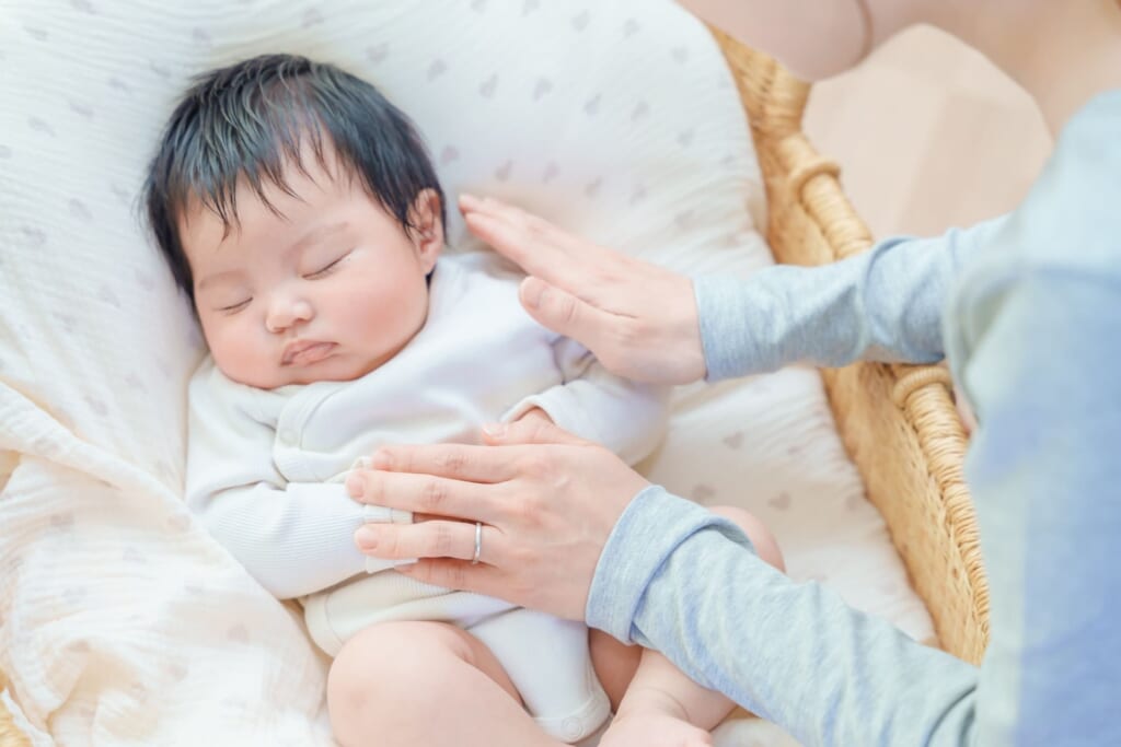 クッションの上で眠る赤ちゃんに優しく手を添える母親