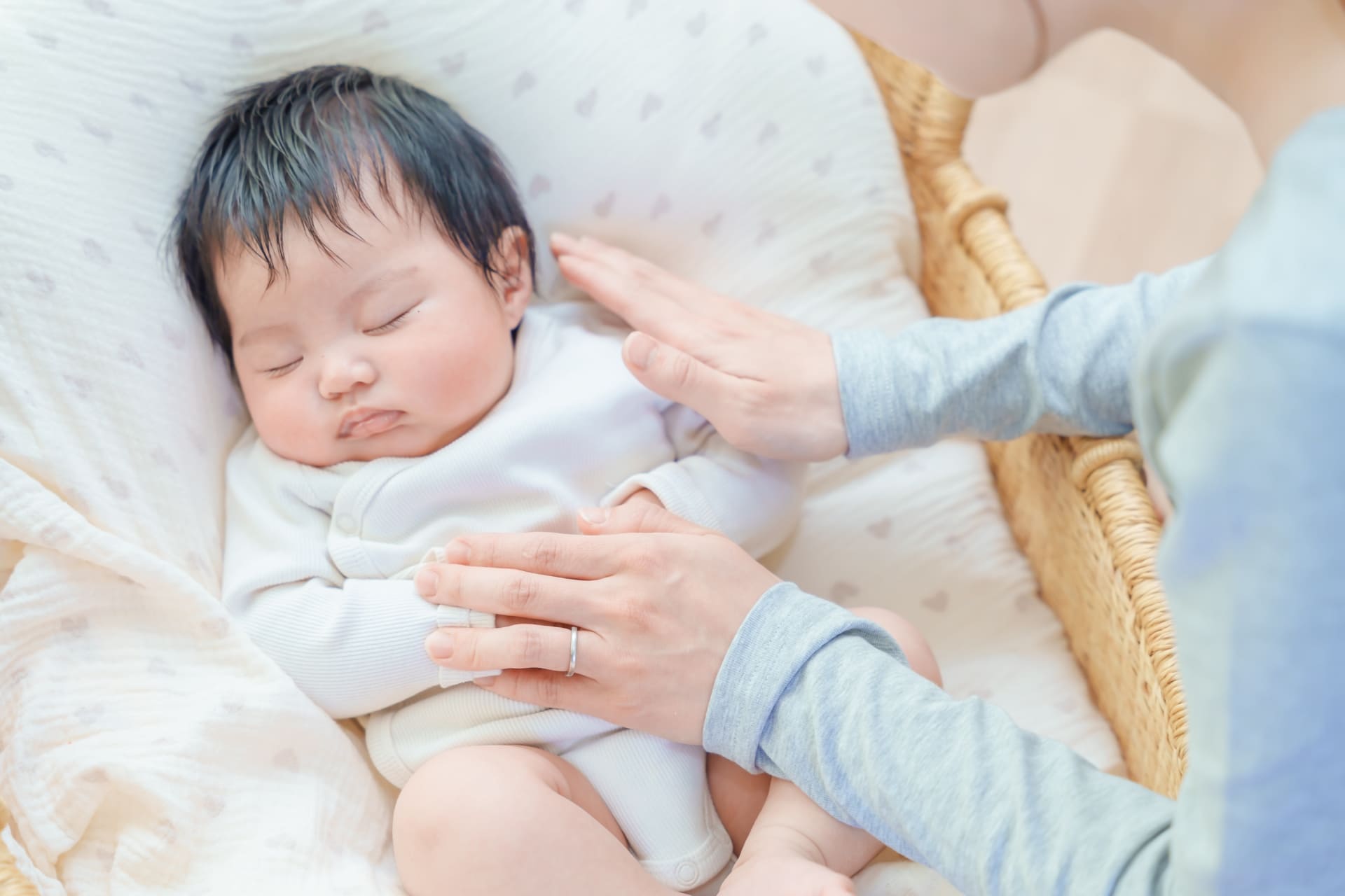 クッションの上で眠る赤ちゃんに優しく手を添える母親