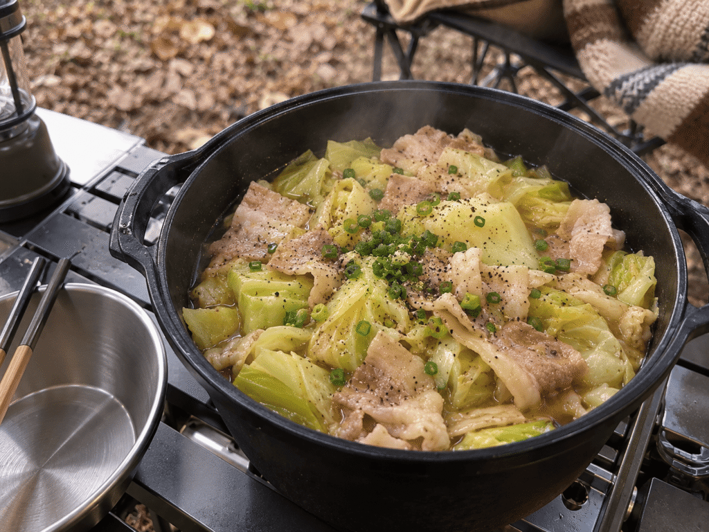 キャンプ用の鍋で豚バラ肉とキャベツを蒸し煮にし、黒こしょうと小ねぎを散らした無水キャベツ鍋