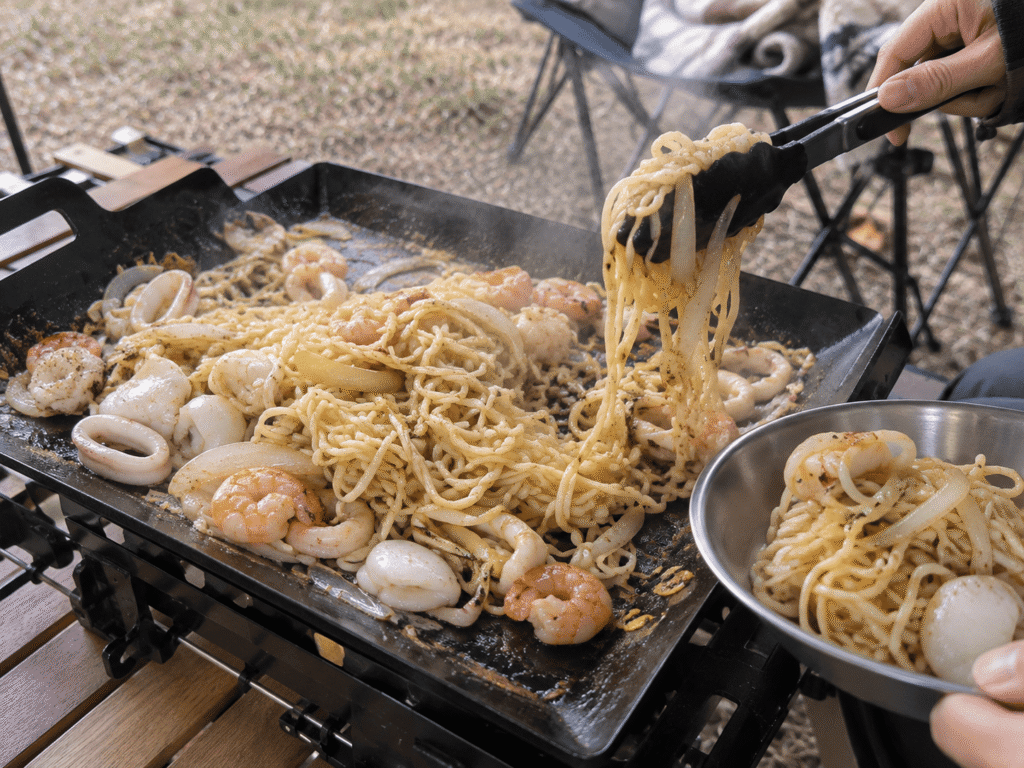 キャンプ用の鉄板でエビやイカなどの魚介と焼きそば麺を炒めた海鮮塩焼きそば